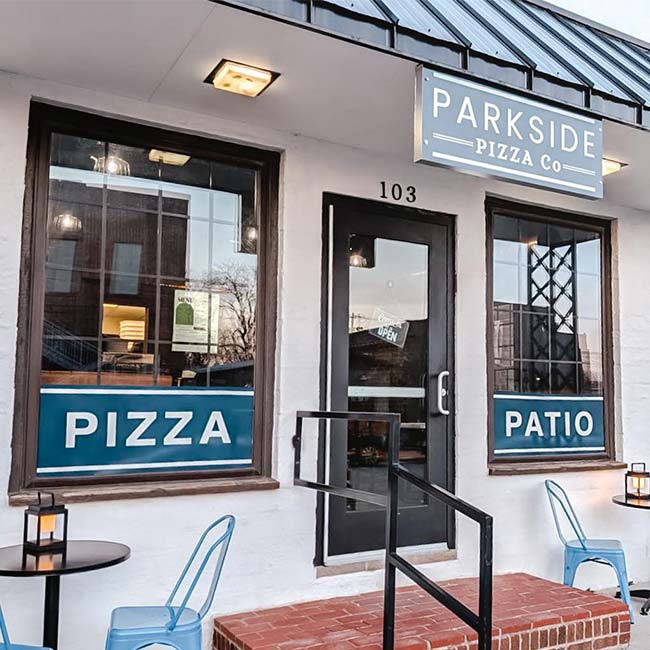 Small pizza restaurant exterior with blue chairs, tables, and signs reading PIZZA and PATIO.