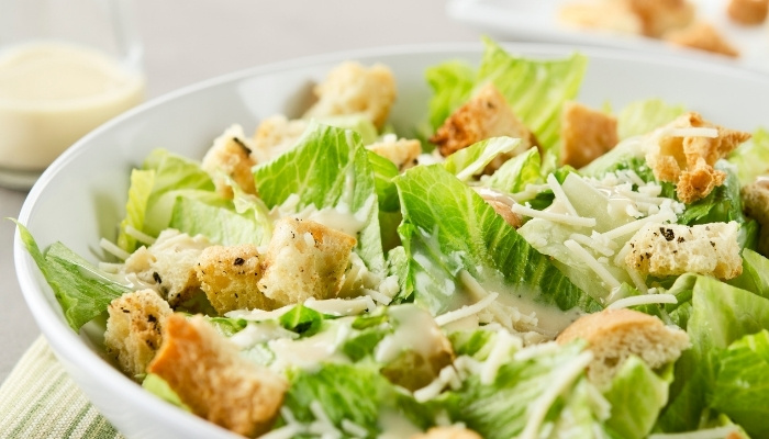 A bowl of Caesar salad with romaine lettuce, croutons, shredded cheese, and dressing.