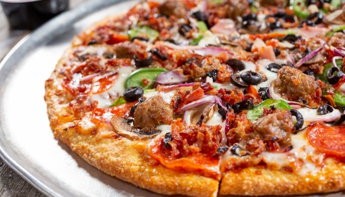 A close-up of a supreme pizza with pepperoni, sausage, olives, onions, and green peppers.