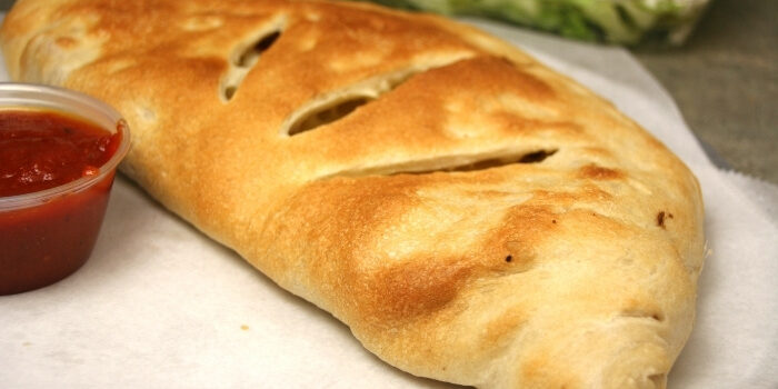 Golden-brown calzone on parchment paper with a cup of marinara sauce on the side.