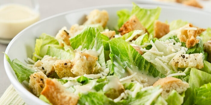 A bowl of Caesar salad with romaine lettuce, croutons, shredded cheese, and dressing.